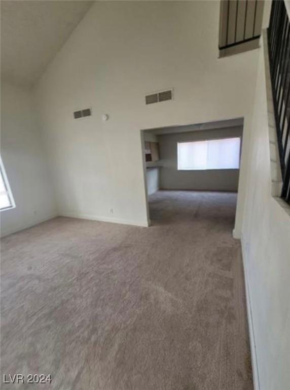 unfurnished living room featuring high vaulted ceiling, a healthy amount of sunlight, and carpet floors