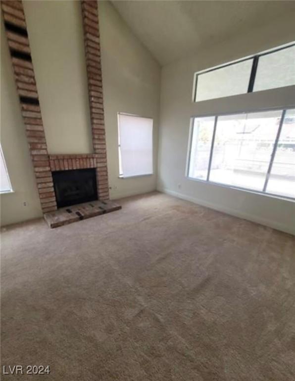 unfurnished living room featuring a brick fireplace, high vaulted ceiling, carpet, and brick wall