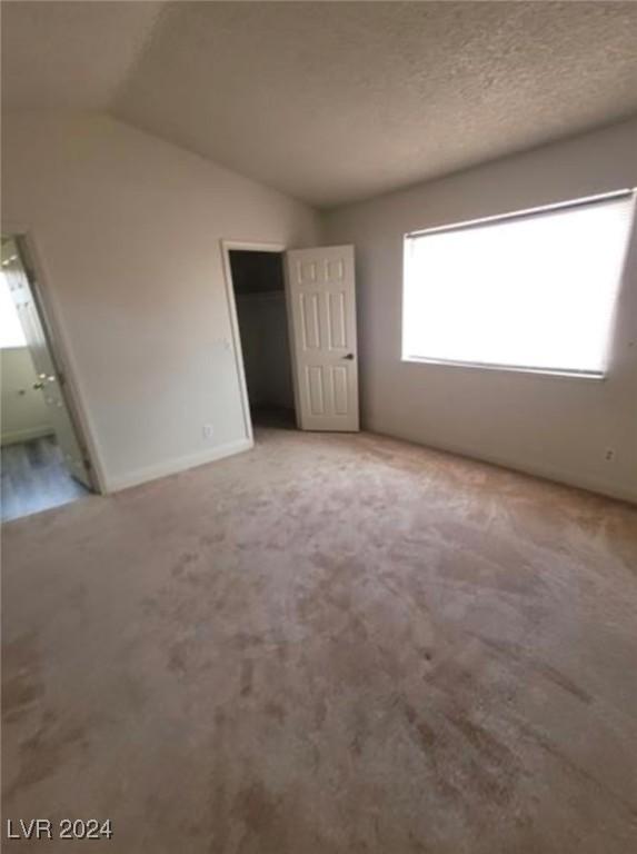 unfurnished bedroom featuring light carpet, a textured ceiling, vaulted ceiling, and ensuite bathroom