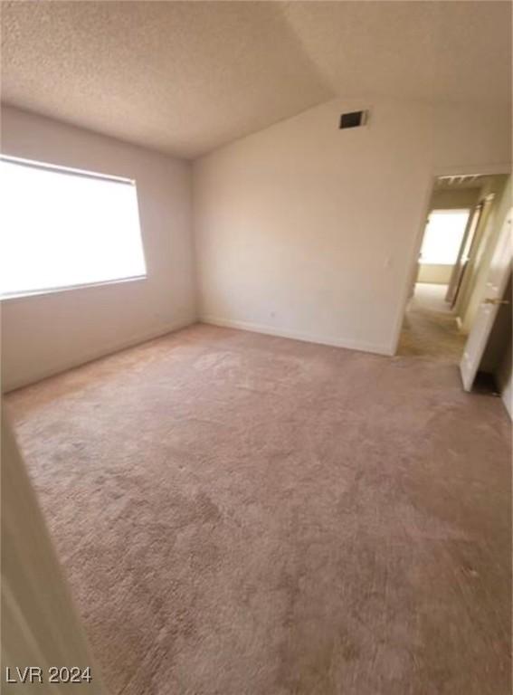 unfurnished room with carpet floors, a textured ceiling, and vaulted ceiling