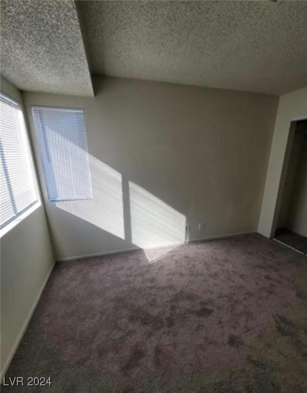 spare room with a textured ceiling and dark carpet