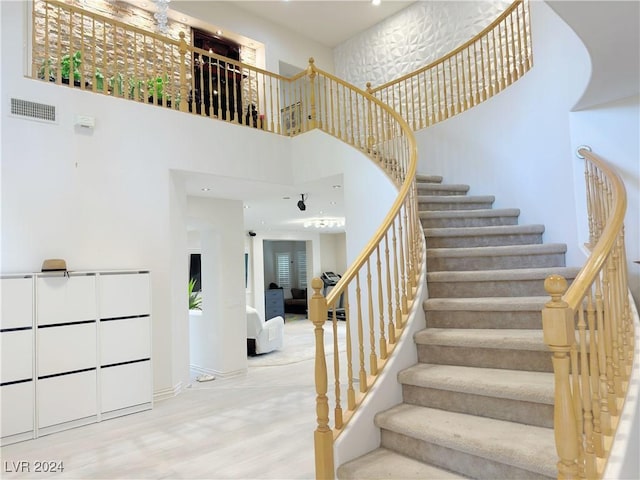 staircase with visible vents, wood finished floors, and a towering ceiling