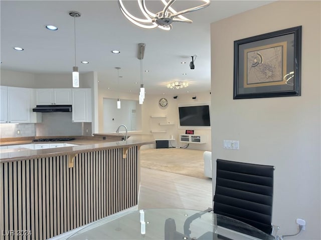 kitchen featuring decorative light fixtures, decorative backsplash, open floor plan, white cabinets, and under cabinet range hood