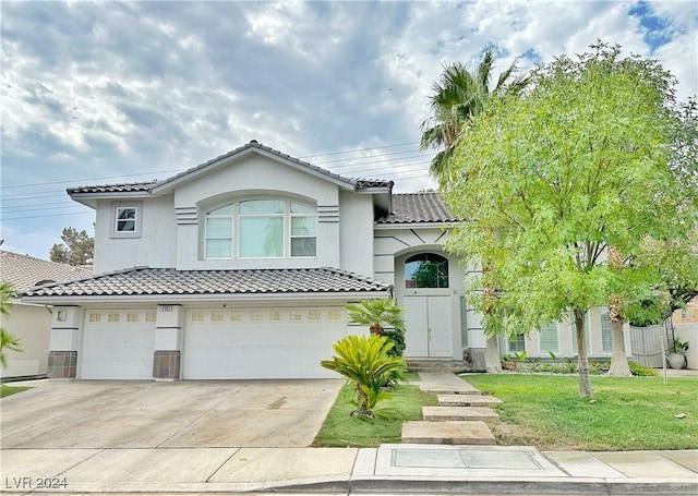 mediterranean / spanish house featuring a garage, concrete driveway, a tile roof, a front lawn, and stucco siding