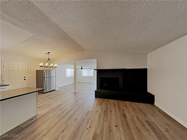 unfurnished living room featuring light hardwood / wood-style flooring, a fireplace, a chandelier, and a textured ceiling