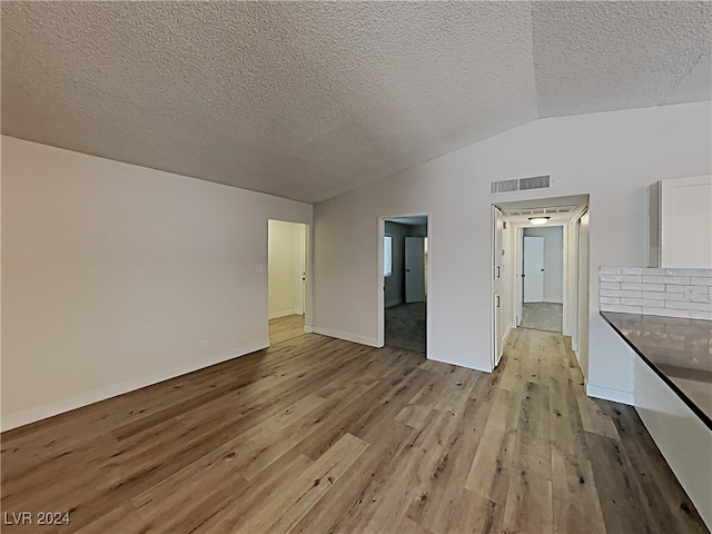 interior space featuring a textured ceiling, light wood-type flooring, and vaulted ceiling