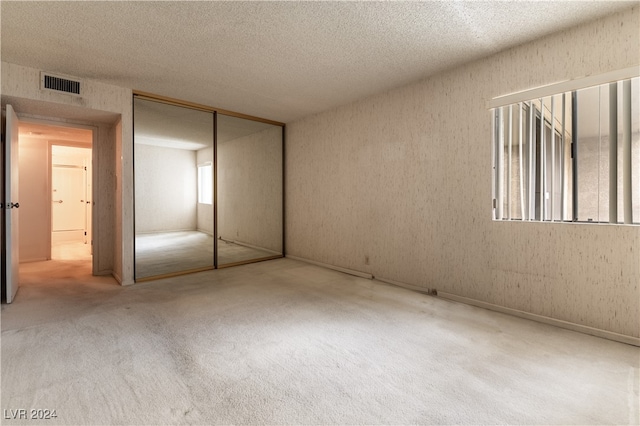 unfurnished bedroom featuring a textured ceiling, light carpet, and a closet