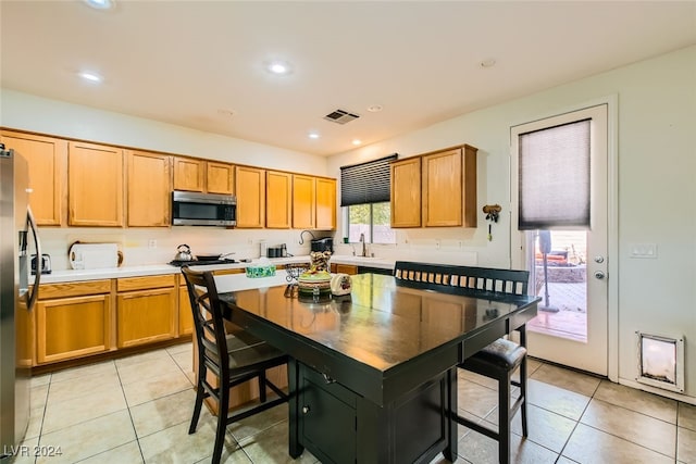 kitchen with sink, a kitchen island, a kitchen breakfast bar, appliances with stainless steel finishes, and light tile patterned floors