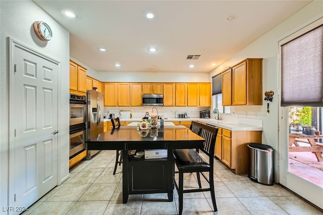 kitchen featuring light tile patterned floors, stainless steel appliances, a kitchen bar, a center island, and sink