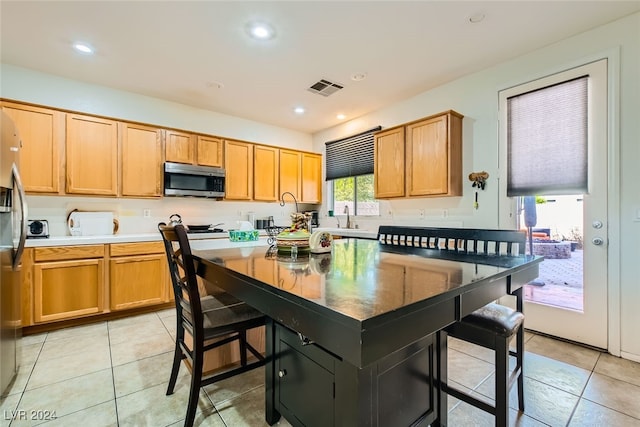 kitchen with sink, a kitchen island, a kitchen breakfast bar, appliances with stainless steel finishes, and light tile patterned floors