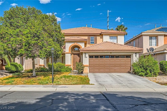 mediterranean / spanish house with a garage, driveway, a tile roof, and stucco siding