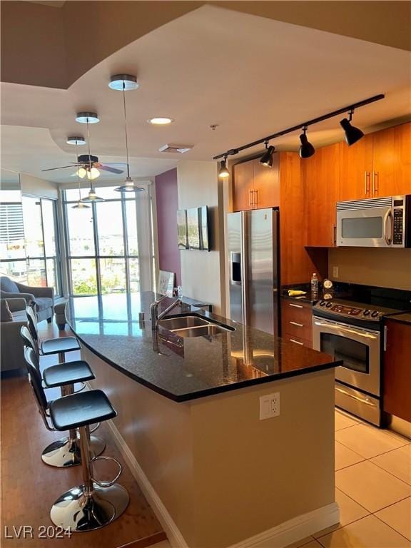 kitchen featuring a breakfast bar, light tile patterned floors, appliances with stainless steel finishes, a sink, and an island with sink