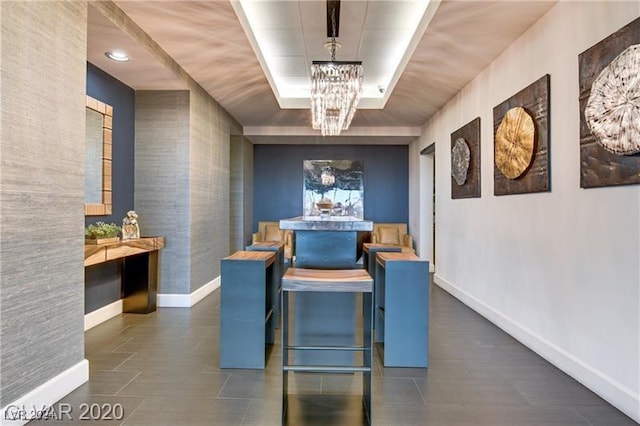 dining space featuring a chandelier, wallpapered walls, a raised ceiling, and baseboards