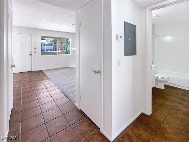 hall featuring dark tile patterned floors, electric panel, and a textured ceiling