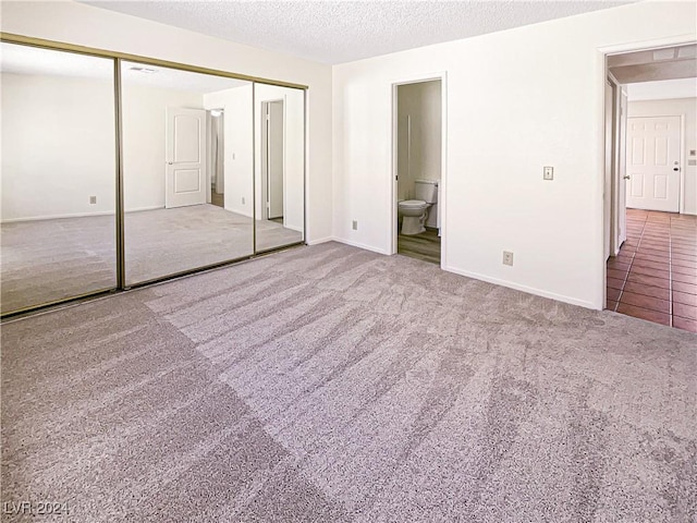 unfurnished bedroom with ensuite bathroom, carpet, a textured ceiling, and a closet