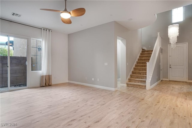 unfurnished living room featuring baseboards, visible vents, a ceiling fan, stairway, and light wood-type flooring