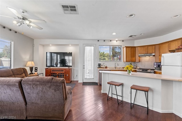 kitchen featuring white refrigerator, stainless steel range, ceiling fan, dark wood-type flooring, and a kitchen bar