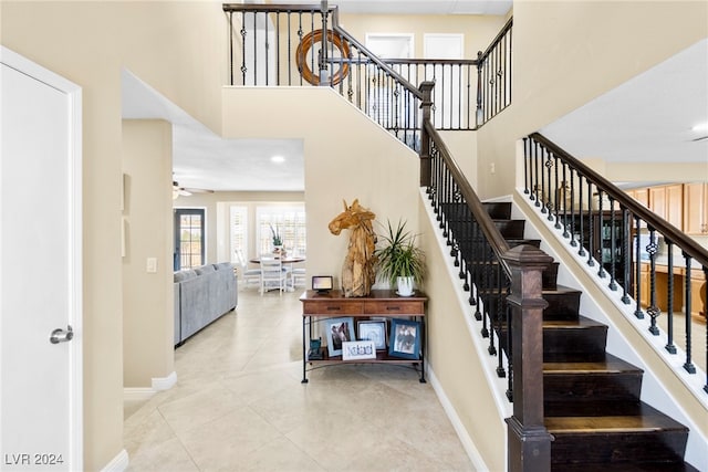 staircase with ceiling fan, tile patterned floors, and a high ceiling