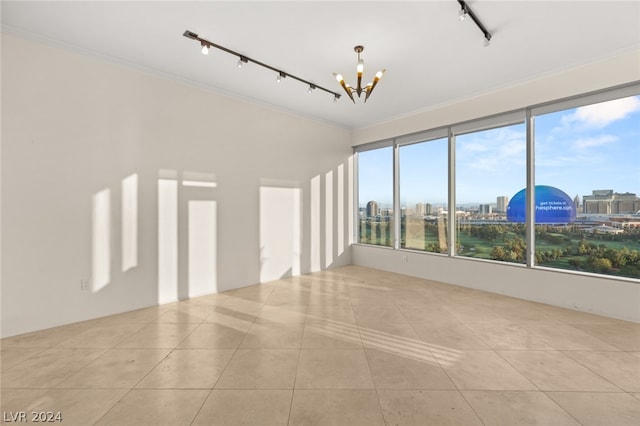 tiled empty room featuring ornamental molding, an inviting chandelier, and track lighting