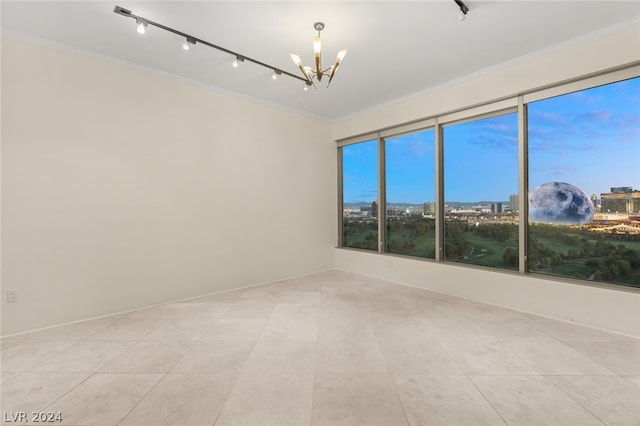 empty room featuring a notable chandelier, light tile patterned floors, track lighting, and ornamental molding