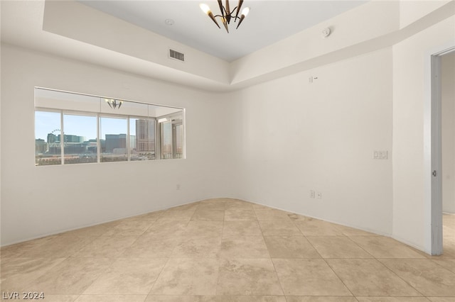 tiled spare room featuring a tray ceiling and an inviting chandelier