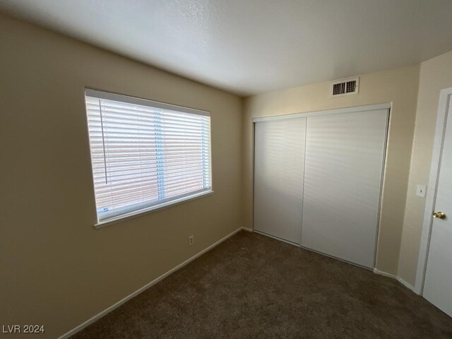 unfurnished bedroom featuring dark carpet and a closet