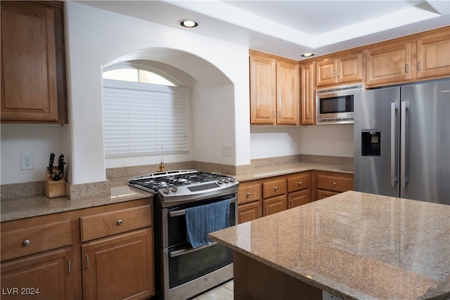 kitchen featuring appliances with stainless steel finishes, a raised ceiling, and light stone countertops