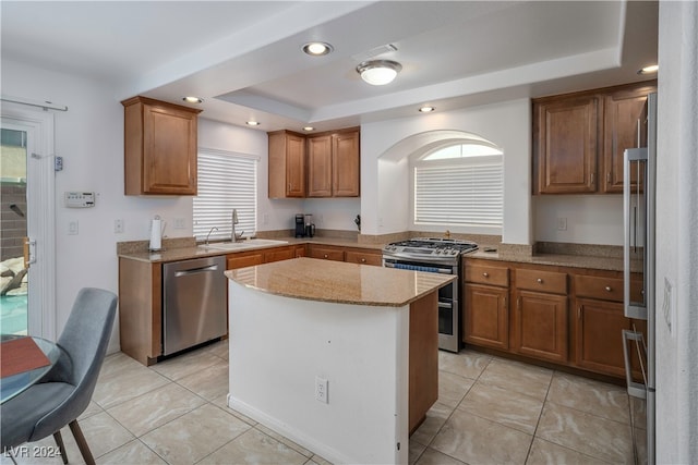 kitchen with stainless steel appliances, light stone countertops, light tile patterned floors, sink, and a kitchen island