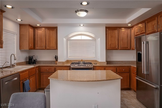 kitchen featuring appliances with stainless steel finishes, a tray ceiling, a center island, and light stone countertops