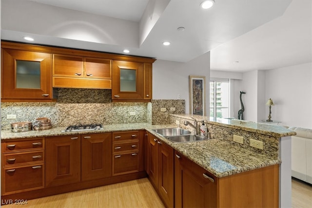 kitchen featuring light wood-type flooring, light stone counters, sink, kitchen peninsula, and tasteful backsplash