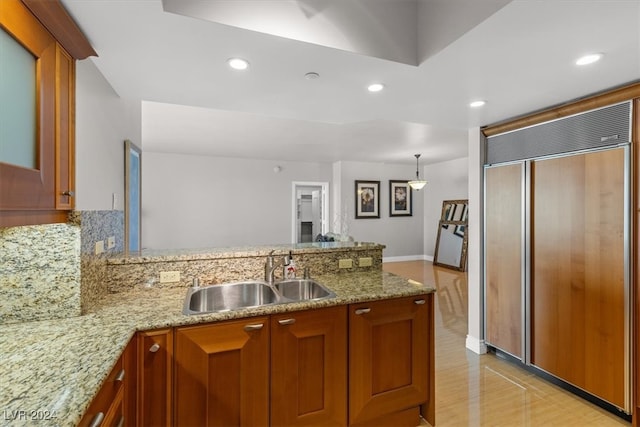 kitchen with paneled refrigerator, light stone counters, kitchen peninsula, and sink