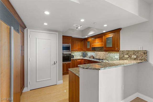 kitchen with backsplash, light stone counters, light hardwood / wood-style floors, kitchen peninsula, and built in appliances