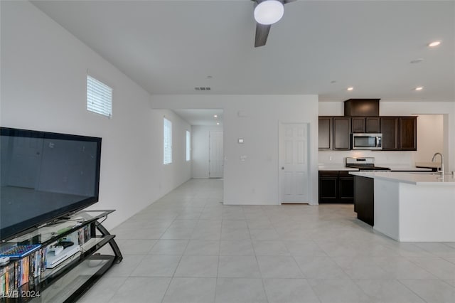 kitchen with an island with sink, ceiling fan, stainless steel appliances, dark brown cabinetry, and light tile patterned floors