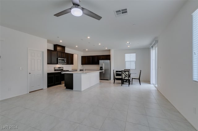 kitchen with appliances with stainless steel finishes, sink, ceiling fan, light tile patterned floors, and a center island with sink