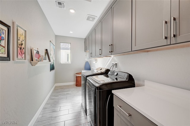 clothes washing area featuring cabinets, washing machine and clothes dryer, and light wood-type flooring