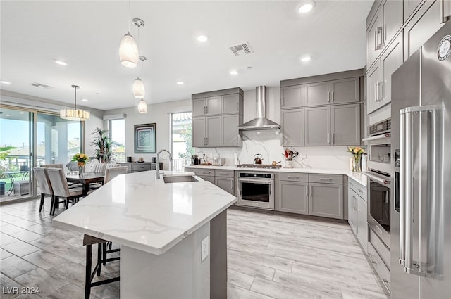 kitchen with decorative light fixtures, sink, a large island, stainless steel appliances, and wall chimney range hood