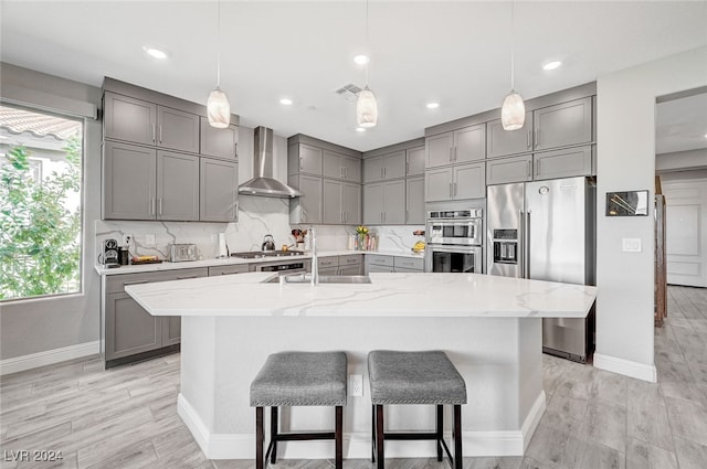 kitchen featuring a spacious island, wall chimney exhaust hood, sink, pendant lighting, and stainless steel appliances