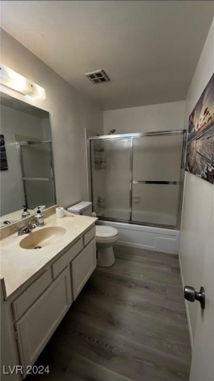 full bathroom with hardwood / wood-style flooring, vanity, combined bath / shower with glass door, and toilet