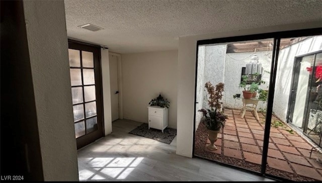 doorway to outside featuring a textured ceiling and light hardwood / wood-style flooring