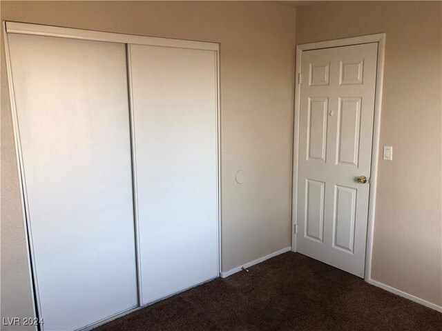 unfurnished bedroom with a closet, dark carpet, and baseboards