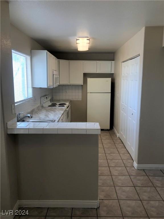 kitchen featuring tile countertops, white cabinetry, light tile patterned flooring, white appliances, and a peninsula