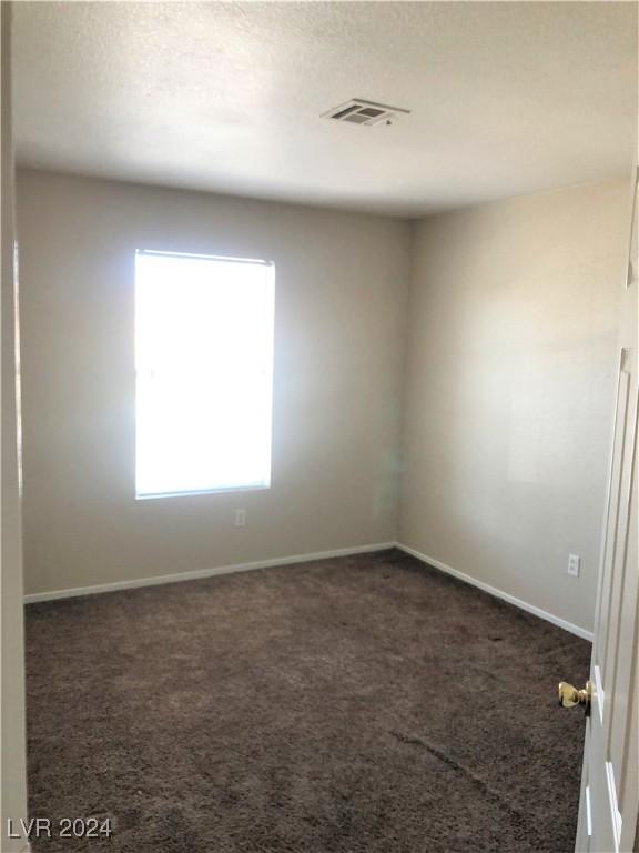 empty room featuring a textured ceiling, carpet floors, visible vents, and baseboards