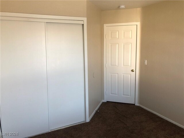 unfurnished bedroom featuring baseboards, dark colored carpet, and a closet