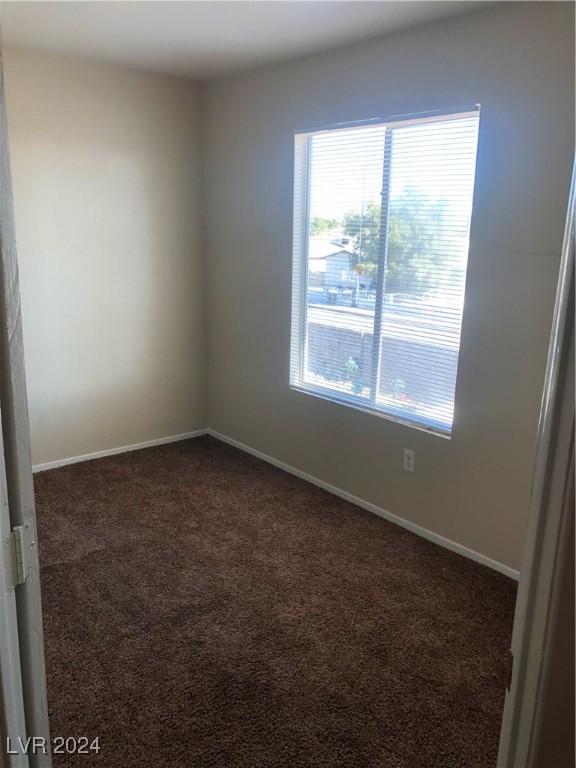 unfurnished room featuring dark carpet and baseboards