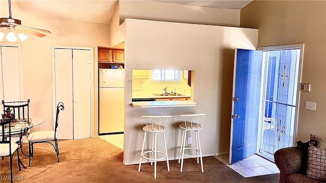 kitchen with sink, a breakfast bar area, white fridge, light colored carpet, and ceiling fan