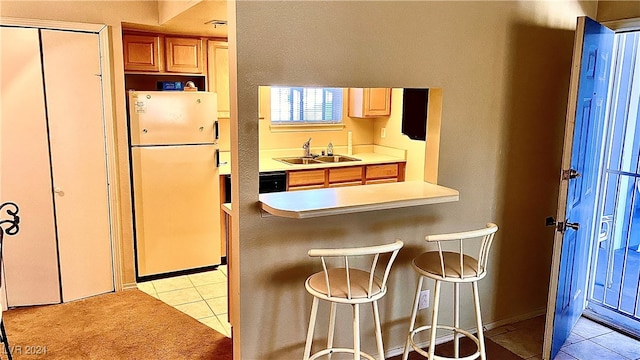 kitchen featuring sink, light tile patterned floors, fridge, and a kitchen breakfast bar