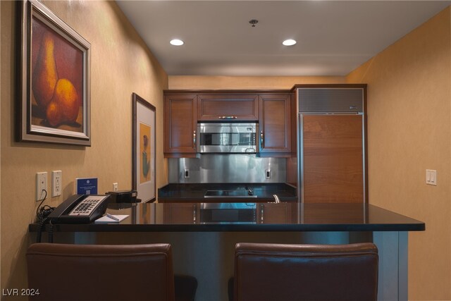 kitchen featuring paneled fridge, a breakfast bar, kitchen peninsula, and black stovetop