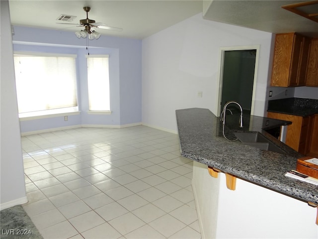 kitchen with ceiling fan, light tile patterned floors, dark stone counters, and sink