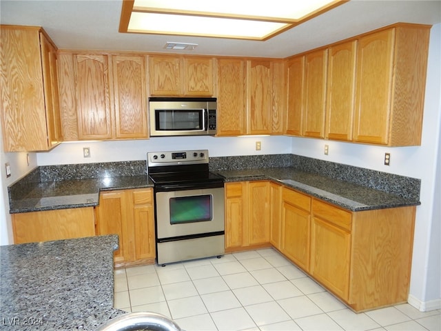 kitchen featuring dark stone countertops, appliances with stainless steel finishes, and light tile patterned floors