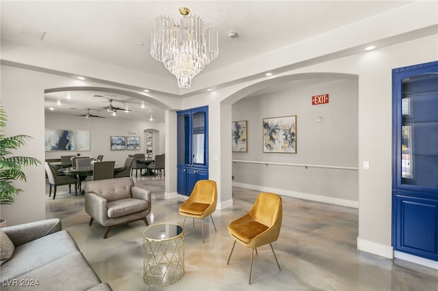 living room with ceiling fan with notable chandelier and concrete flooring